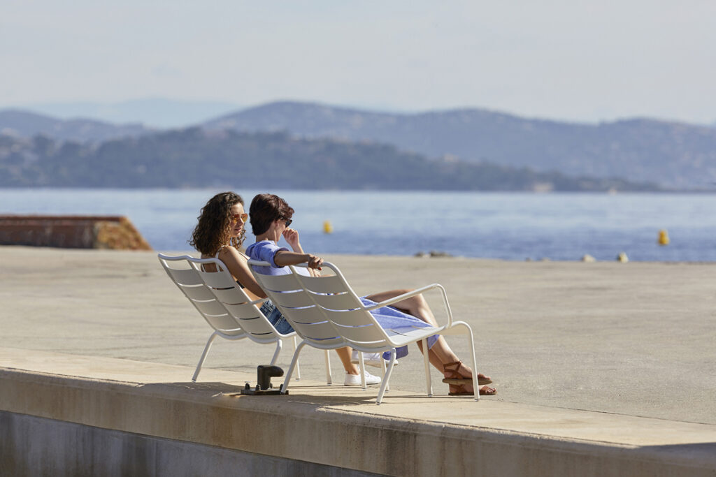 Deux femmes assises sur un Fauteuil bas duo Luxembourg à côté d'un plan d'eau.
