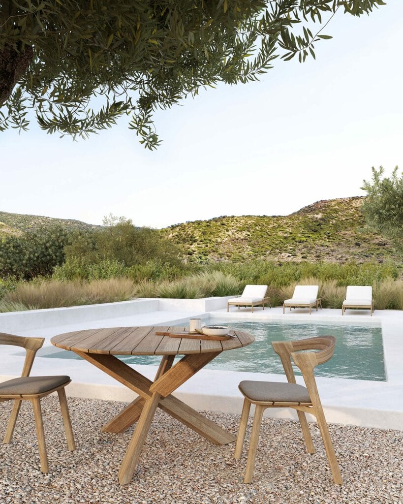 Une Table de jardin Circle en teck et des chaises à côté d'une piscine.
