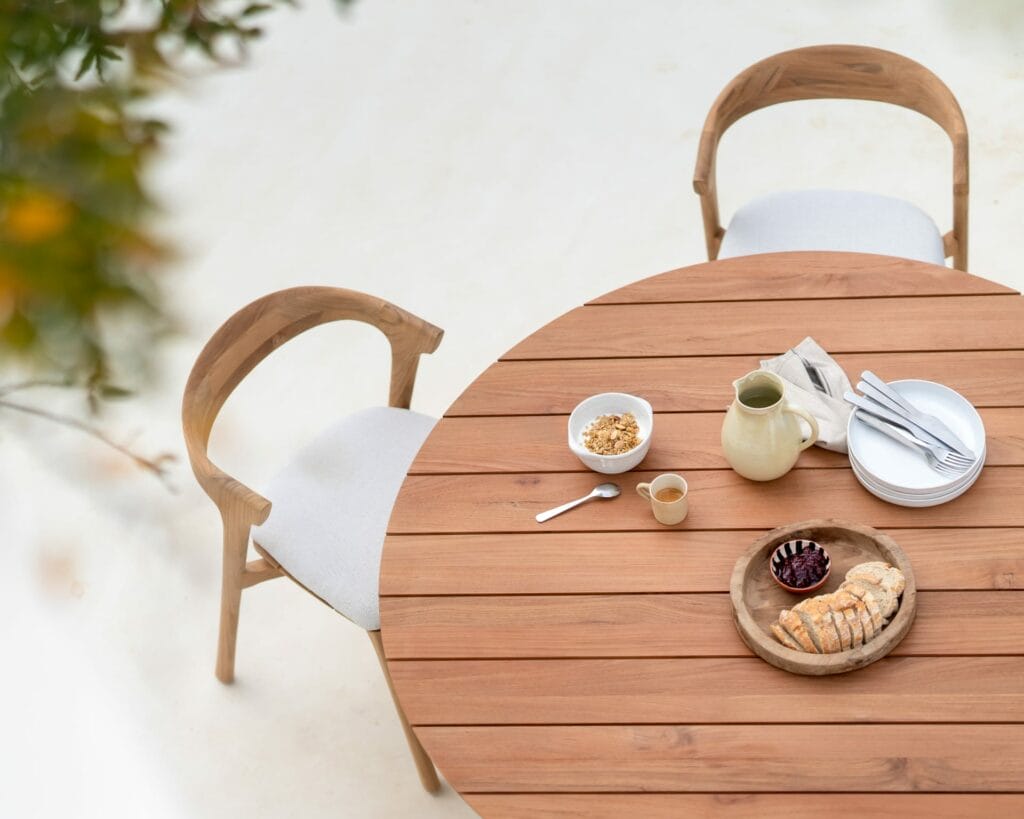 Une table de jardin Circle en teck avec deux chaises et un bol de fruits.
