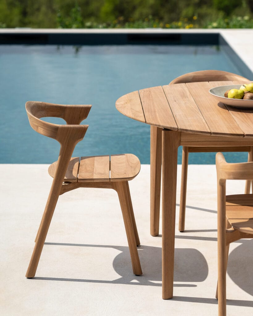Une table à manger en bois et une chaise de jardin Bok en teck près d'une piscine.