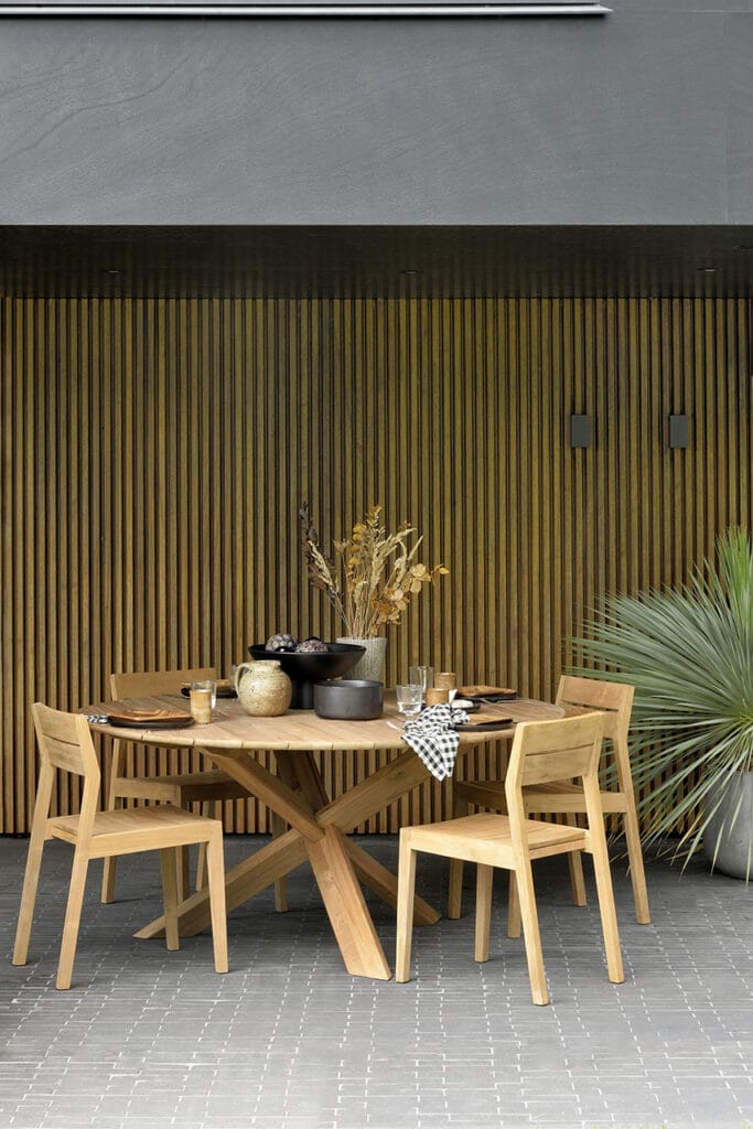 Une table à manger et des chaises en bois sur un patio avec une Chaise de jardin EX1 en teck.