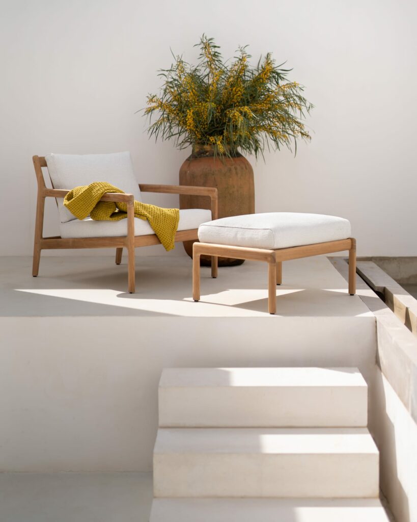 Un fauteuil de jardin Jack en teck et un pot de plante sur un patio blanc.