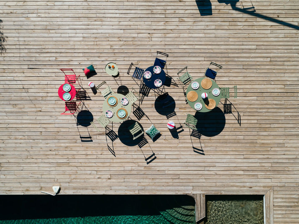 Une Table ronde Bistro, diamètre 117 cm et chaises posées sur une terrasse en bois.