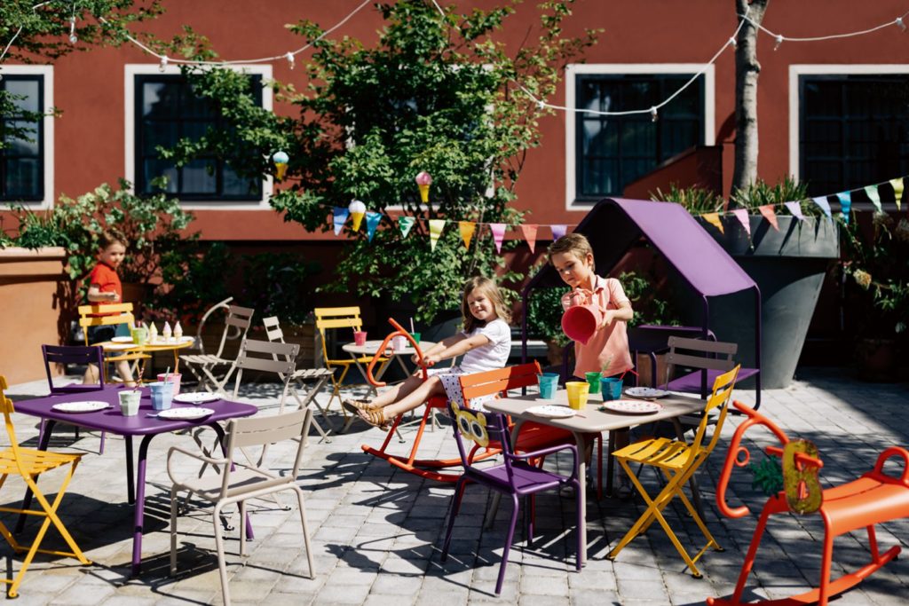 Table enfant luxembourg de jardin 76x55 cm en acier laque sur terrasse au soleil a Paris avec des enfants qui jouent