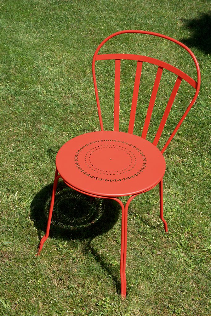 Une chaise en métal rouge dans une zone herbeuse.