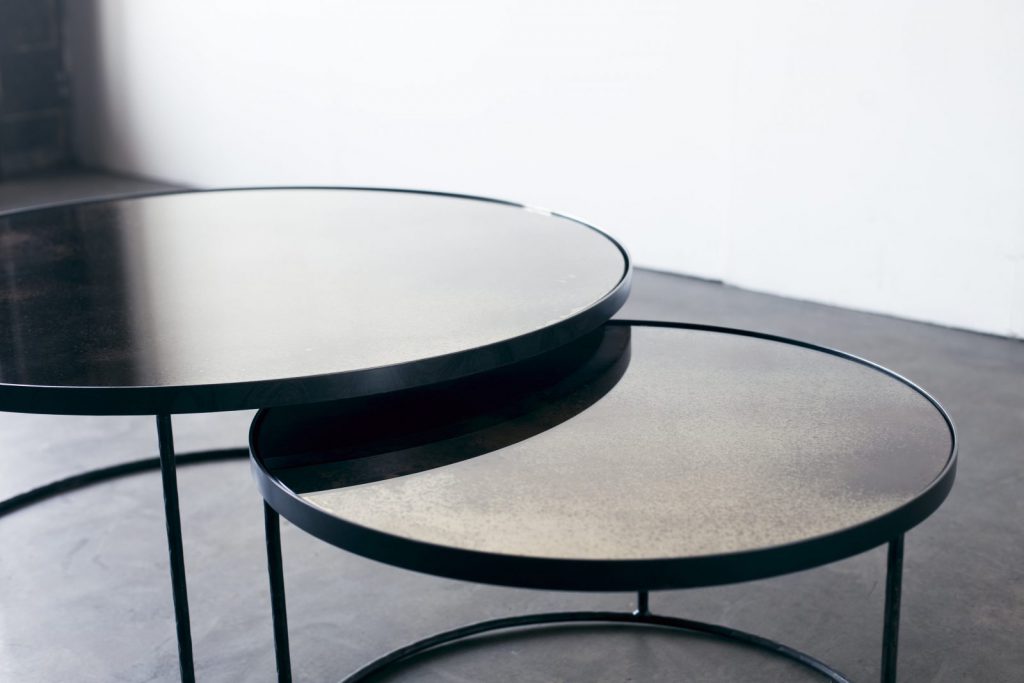 Deux tables rondes avec pieds en métal noir et plateaux en verre.