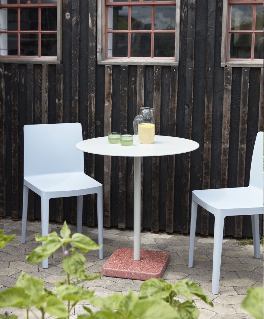 Une table blanche et deux chaises devant un mur de briques.