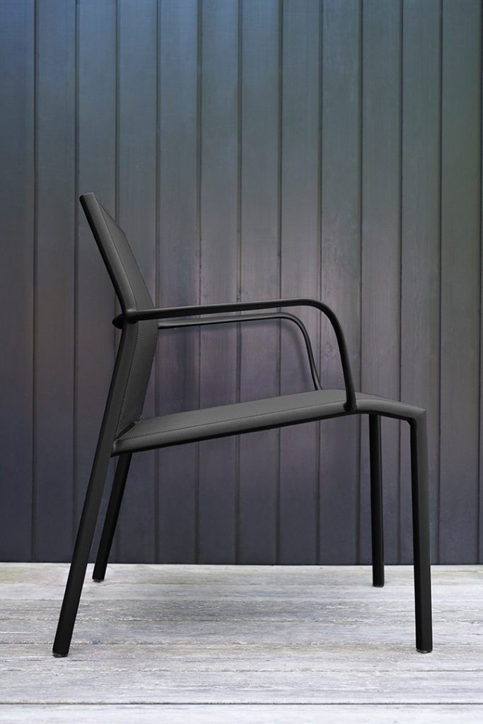 Une chaise longue noire devant un mur en bois.