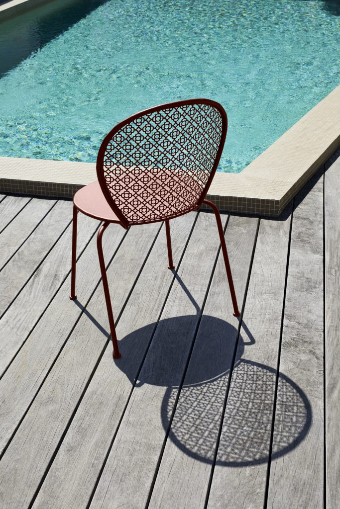 Une chaise rouge sur une terrasse en bois au bord d’une piscine.