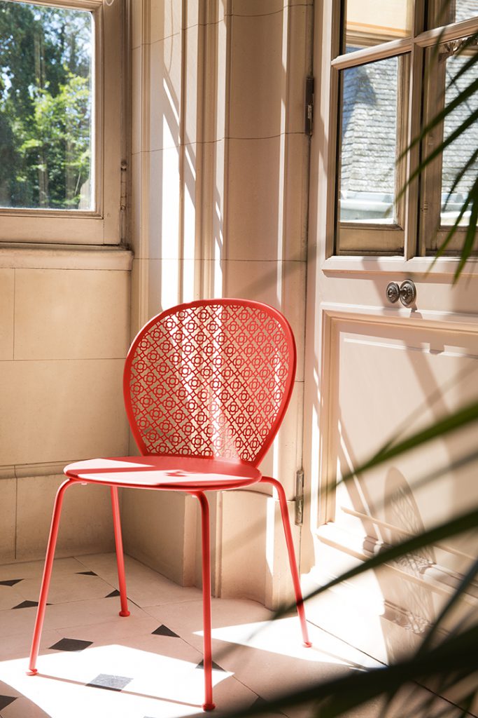 Une chaise rouge est posée sur un sol carrelé devant une fenêtre.