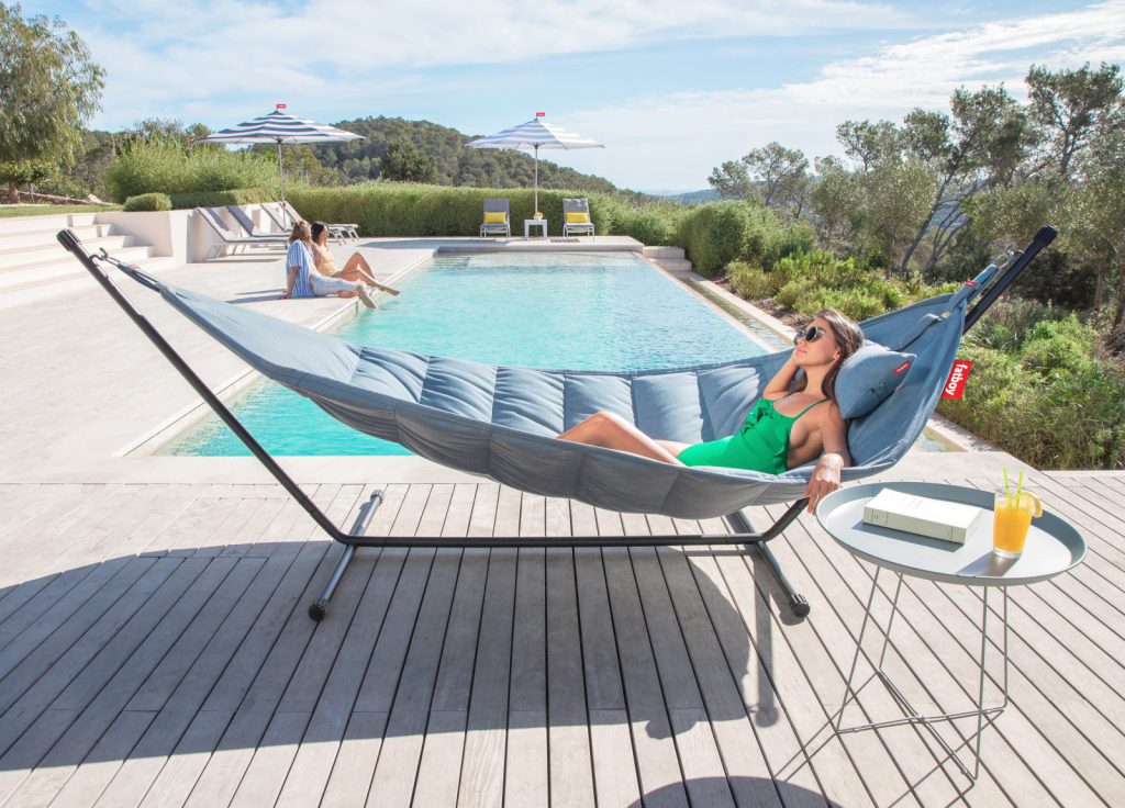 Une femme assise dans un hamac au bord d’une piscine.
