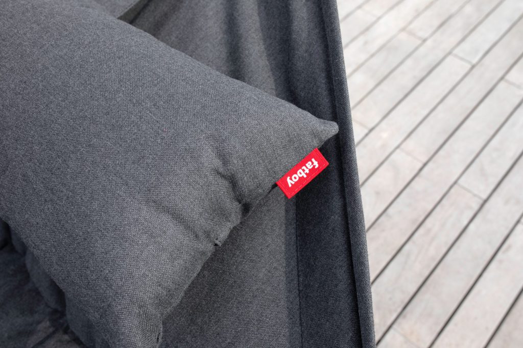 Un oreiller gris avec une étiquette rouge dessus sur une terrasse en bois.