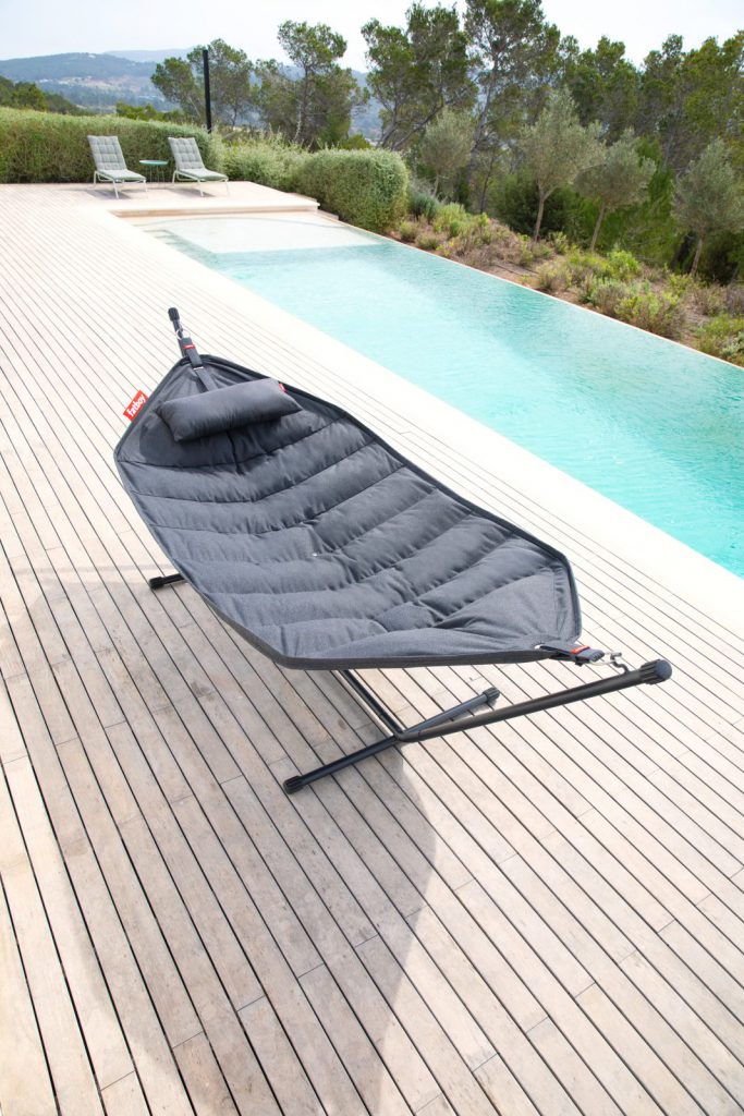 Un hamac noir sur une terrasse en bois au bord d'une piscine.