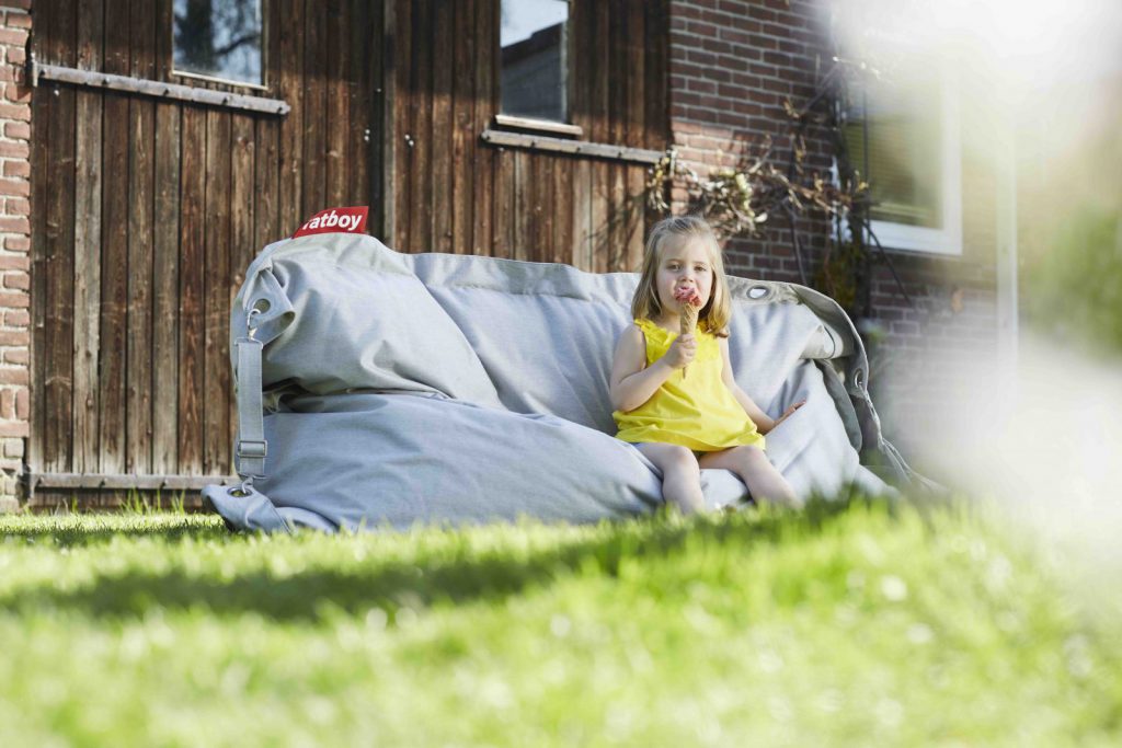Une petite fille assise sur un pouf dans l'herbe.