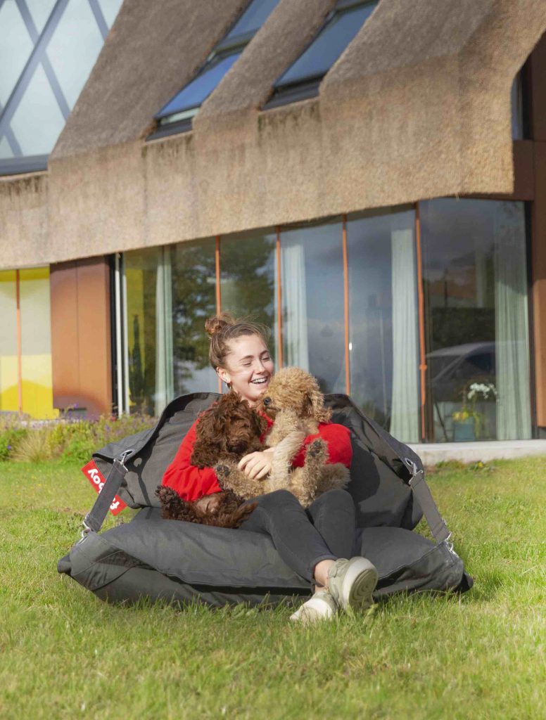 Une femme assise sur un pouf devant une maison.