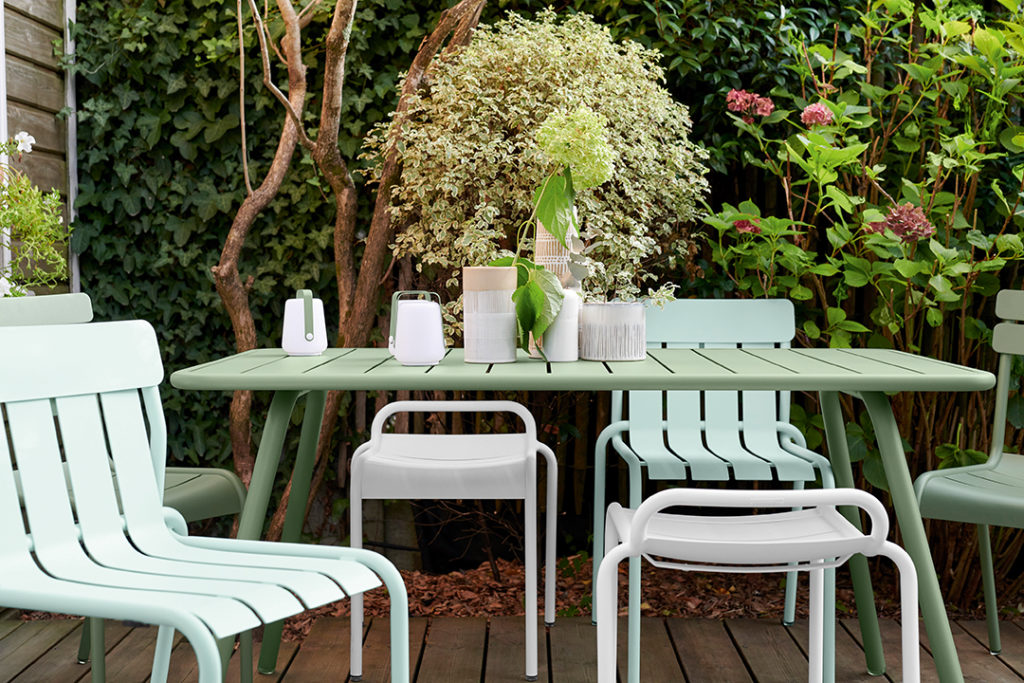 Tabourets bas et table de jardin luxembourg dans les tons vert sur terrasse avec de la verdure autour