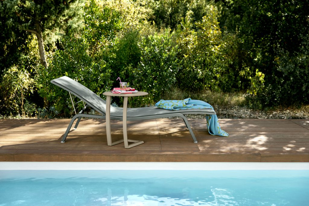 Une chaise longue sur une terrasse en bois au bord d'une piscine.