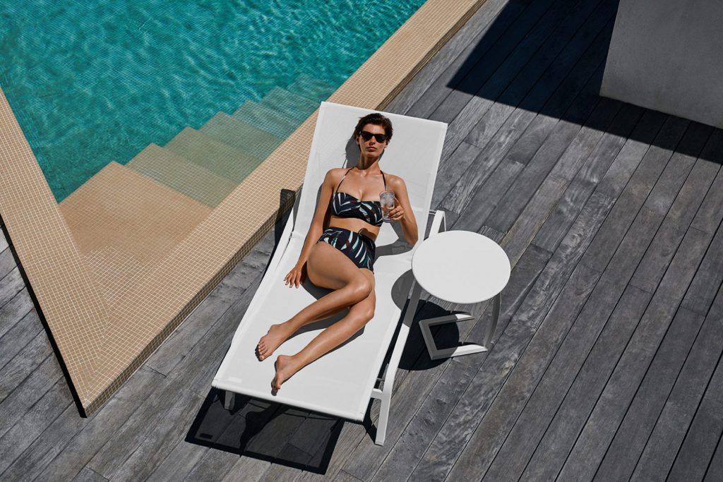 Une femme allongée sur une chaise longue au bord d’une piscine.