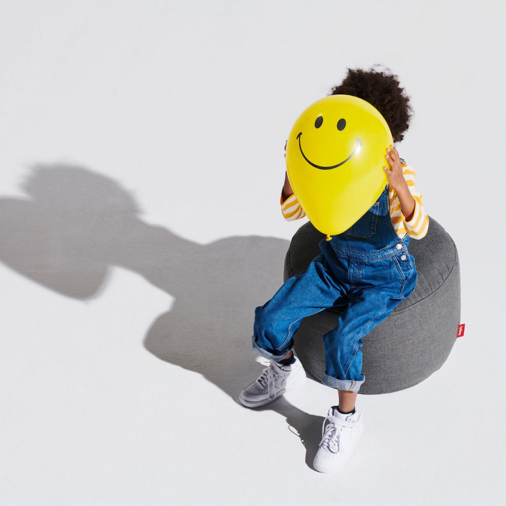 Un enfant assis sur un pouf avec un visage souriant.