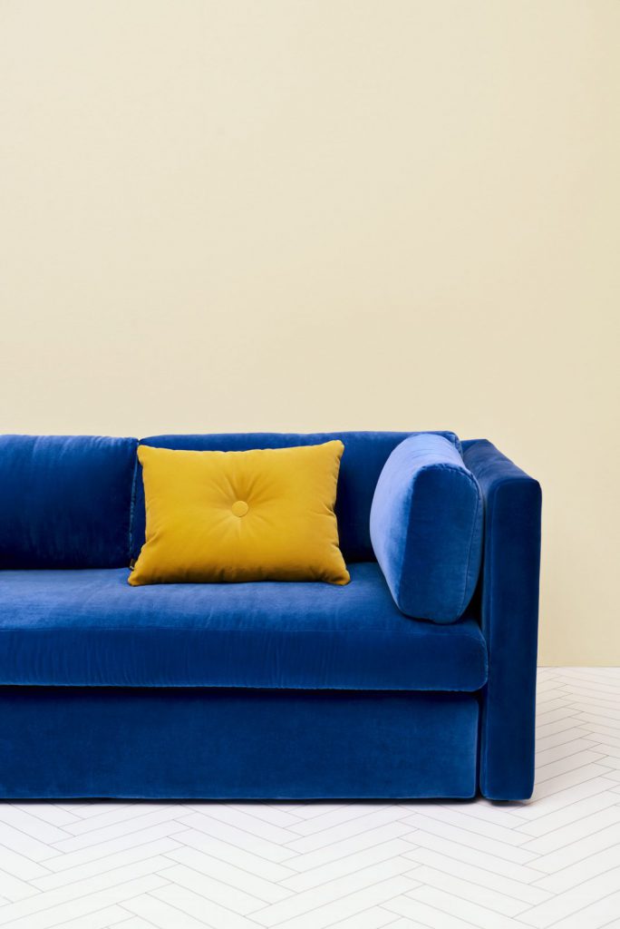 Un canapé en velours bleu avec un oreiller jaune.