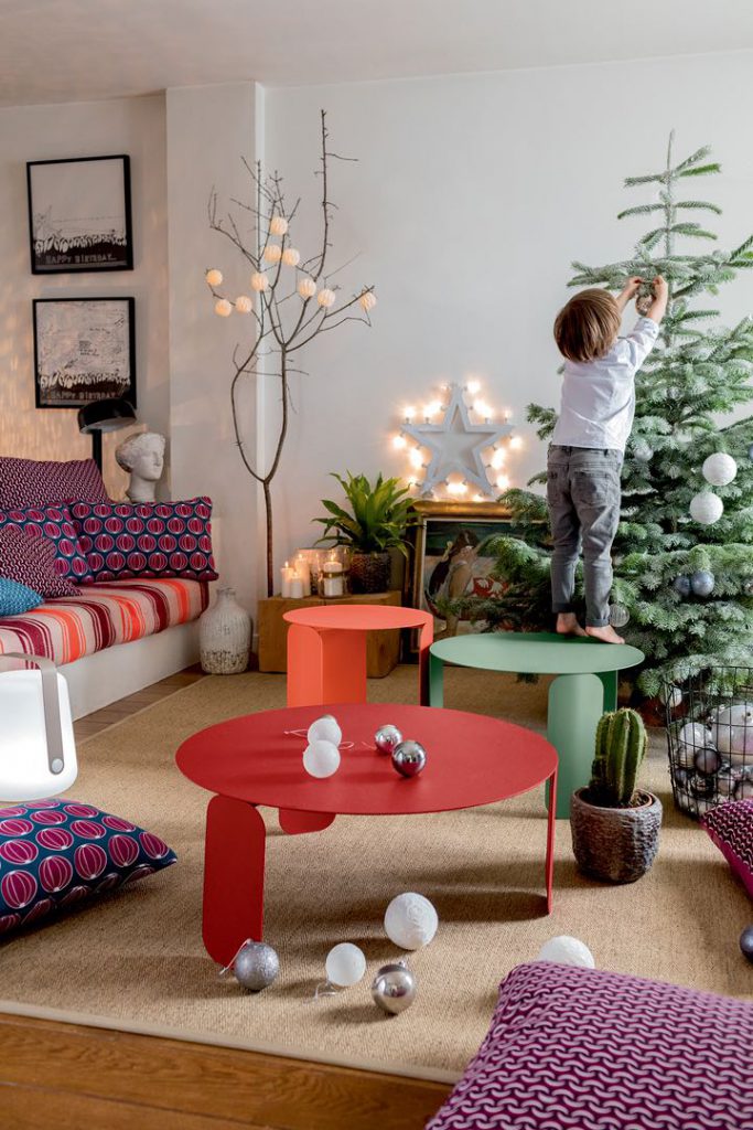 Un enfant se tient à côté d’un sapin de Noël dans un salon.