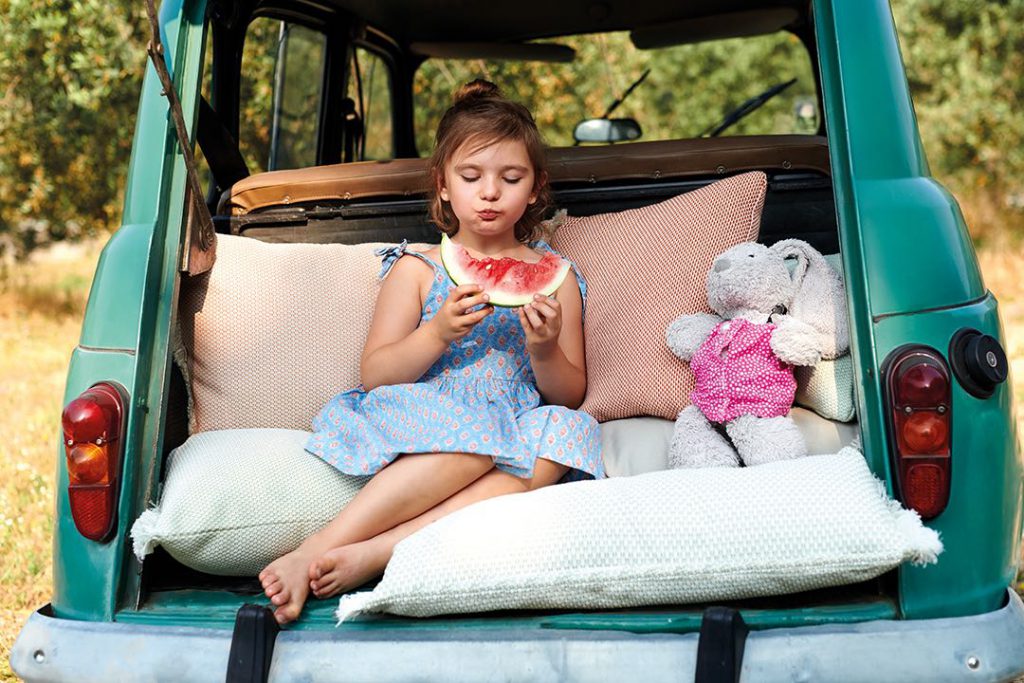 Une petite fille assise sur le siège arrière d’une voiture avec un ours en peluche.
