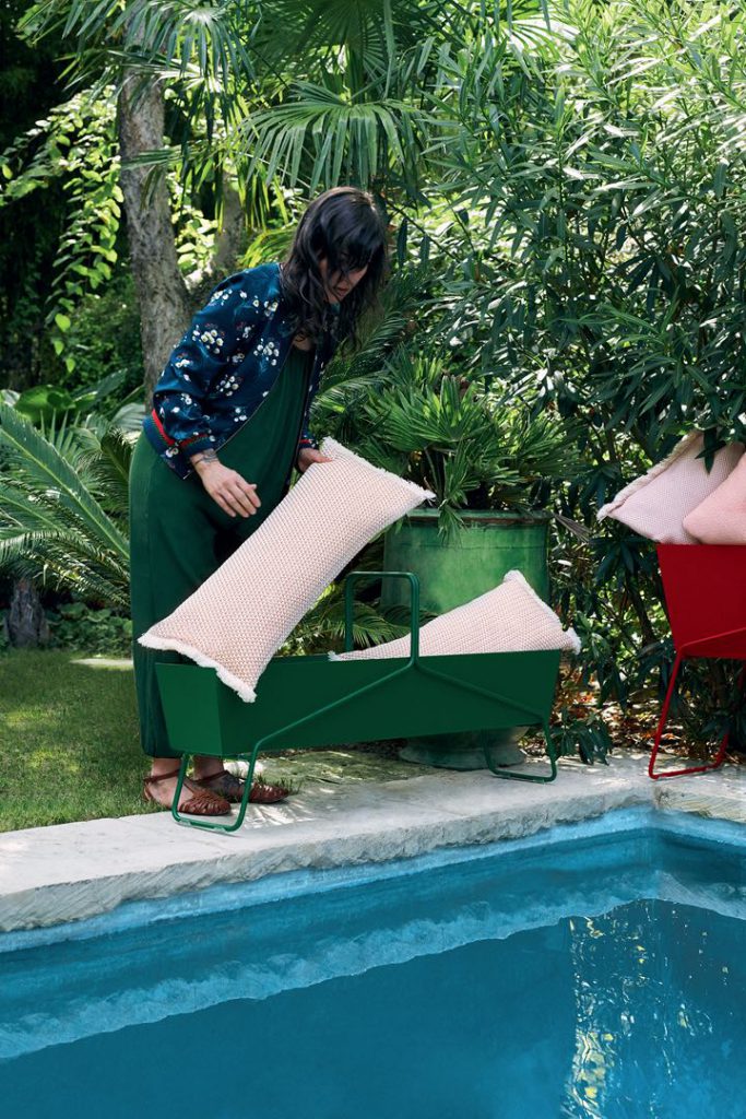 Une femme en tablier vert et un tablier rouge au bord d’une piscine.