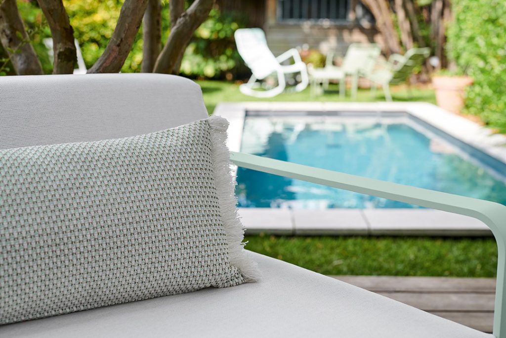 Une chaise blanche avec un oreiller vert devant une piscine.