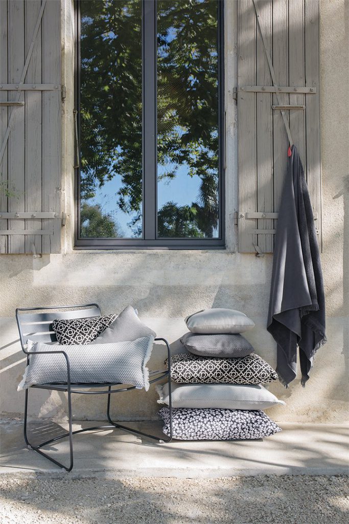 Une chaise avec des oreillers et une fenêtre devant.
