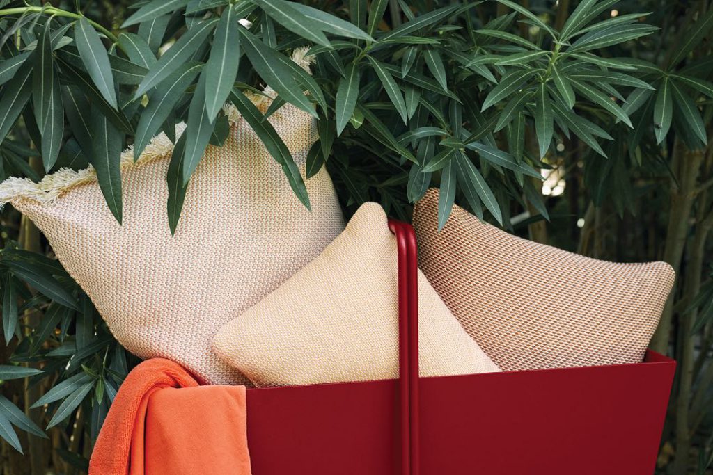 Un panier rouge rempli d'oreillers et de serviettes à côté d'un arbre.