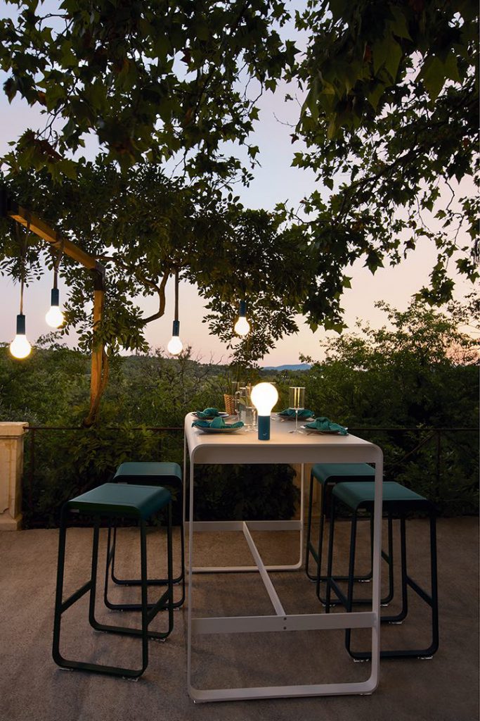 Une table à manger et des chaises sous un arbre au crépuscule.