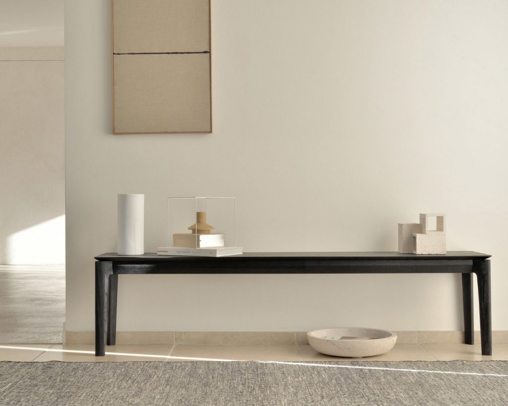 Un banc noir devant un mur blanc.