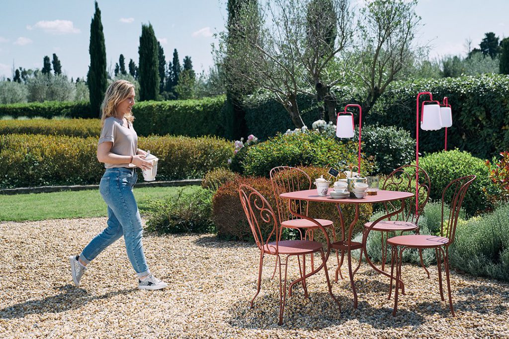 Une femme marchant dans un jardin avec une table et des chaises.