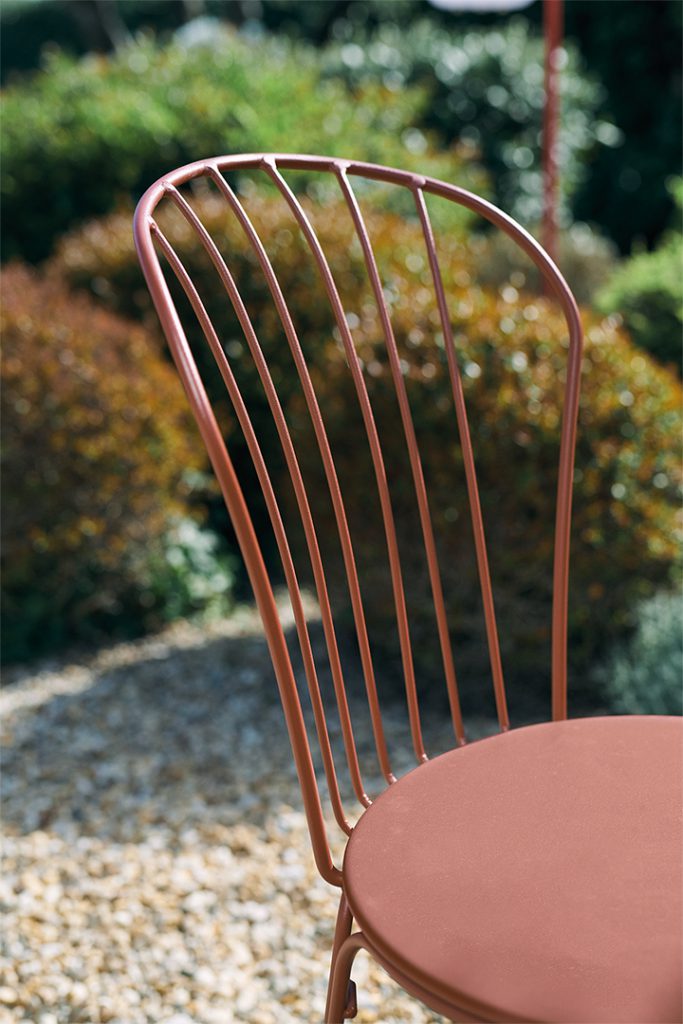 Une chaise en métal avec un siège rouge dans un jardin.