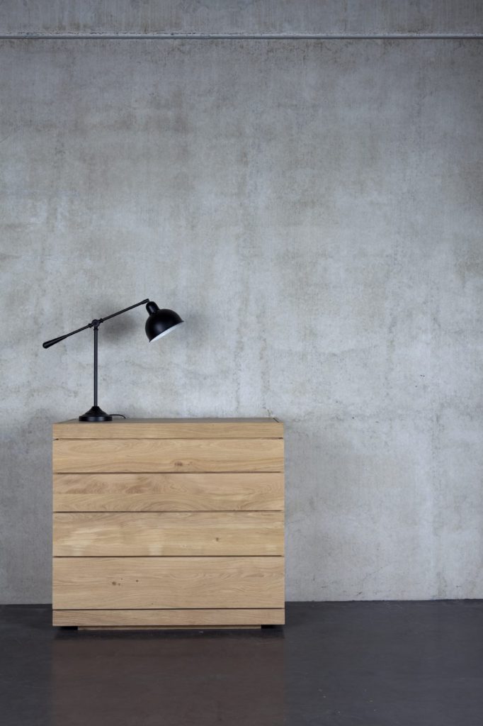 Une commode en bois avec une lampe devant un mur en béton.