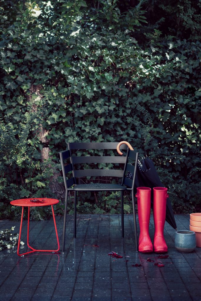 Une chaise avec un parapluie rouge et une paire de bottes de pluie rouges.