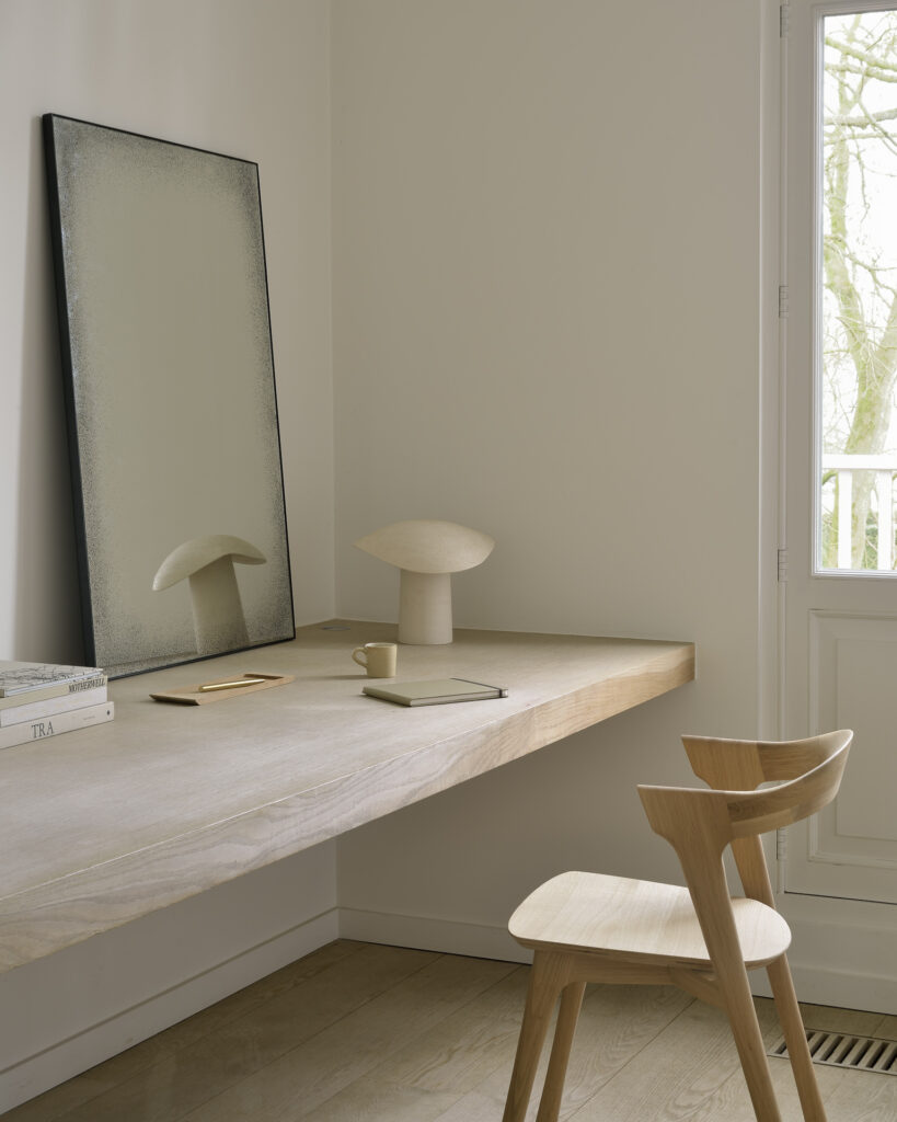 Un bureau en bois dans une pièce avec un miroir et une chaise Bok en chêne.