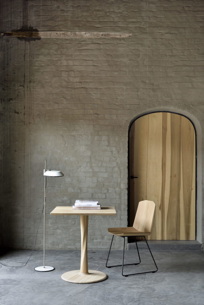 Une Table Torsion carrée en chêne dans une pièce avec un mur en brique.