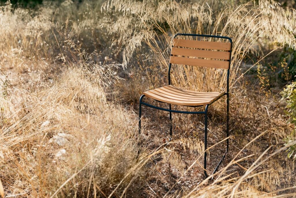 Une chaise solitaire Surprenante chaise en teck au milieu d'herbes hautes et sèches dans un cadre naturel baigné de doux soleil.