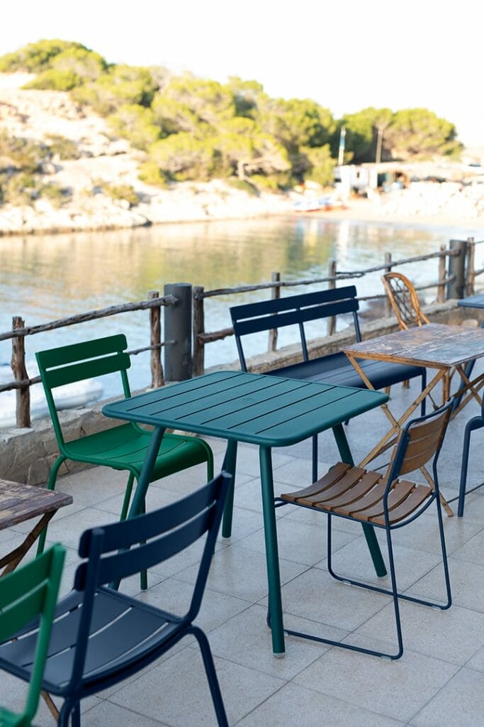 Coin repas extérieur avec chaises et tables colorées en teck. Surprenantes chaises et tables donnant sur une baie tranquille avec des arbres et un ciel dégagé.