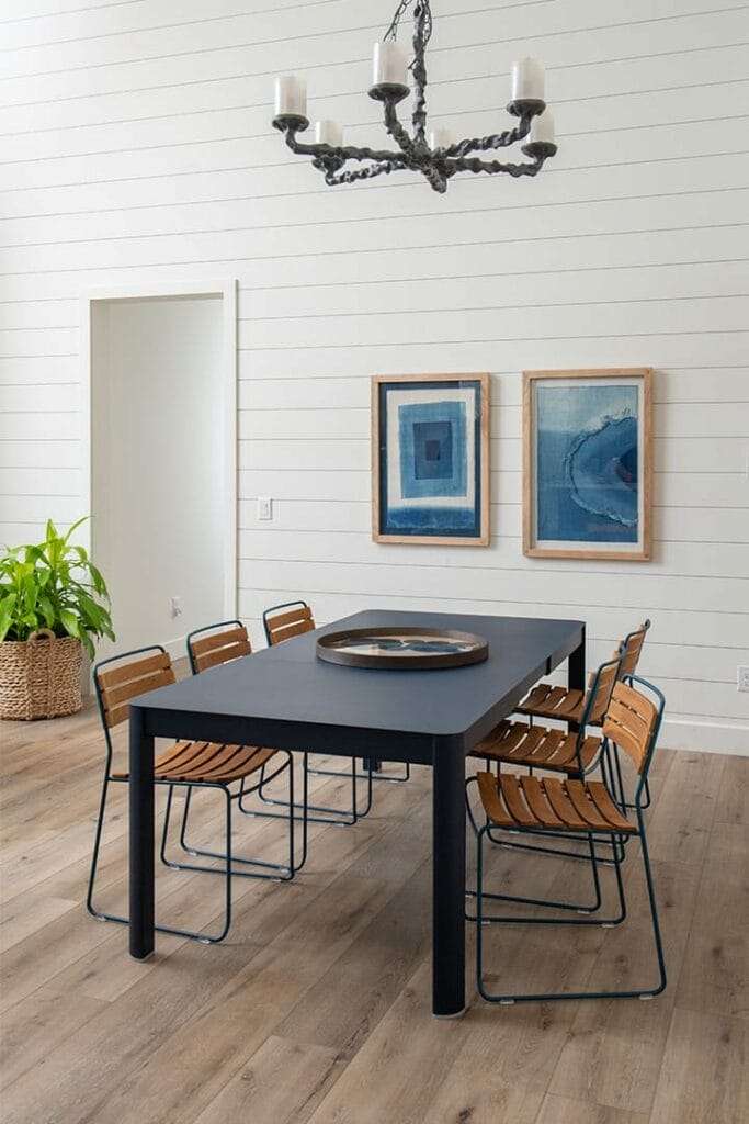 Salle à manger moderne avec une table noire, des chaises en teck surprenantes en métal, deux tableaux abstraits bleus et un lustre rustique.