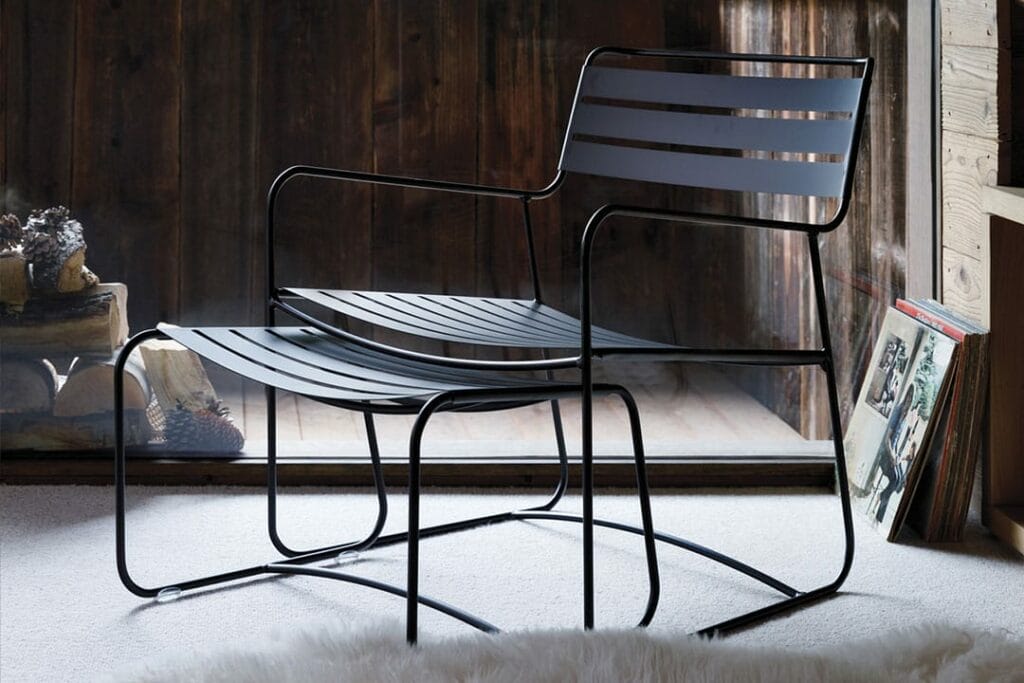 Une chaise Eames Lounge moderne avec des lattes horizontales, à côté d'une petite pile de livres sur un tapis blanc, sur un fond de mur en bois.