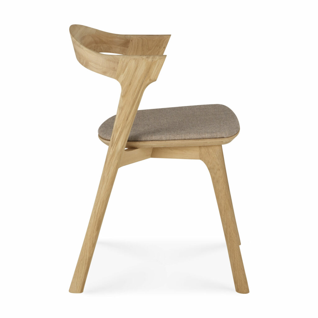 Vue de côté d'une chaise en bois moderne, rappelant la Chaise Bok en chêne, assise en tissu, avec un dossier incurvé et une assise rembourrée. La chaise est dotée d'une finition en bois clair et d'un revêtement en tissu gris clair sur l'assise.