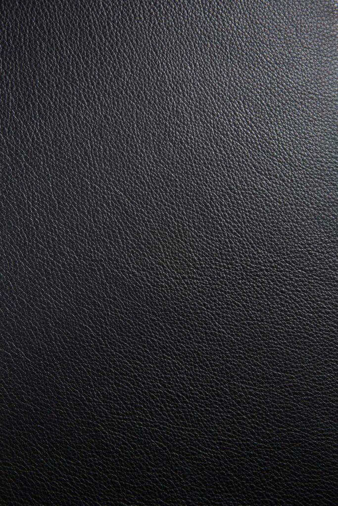 Gros plan sur un cuir texturé noir. La surface présente un motif de grain uniforme, typique du cuir véritable souvent utilisé dans les tissus d'ameublement ou les accessoires de mode comme la Chaise Bok en chêne noir, assise en cuir.