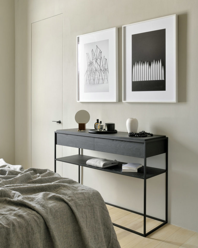 Une console Monolit en chêne noir, réalisée en bois de chêne, complète avec élégance l'intérieur de la chambre aux côtés d'un lit douillet et d'une table de chevet.