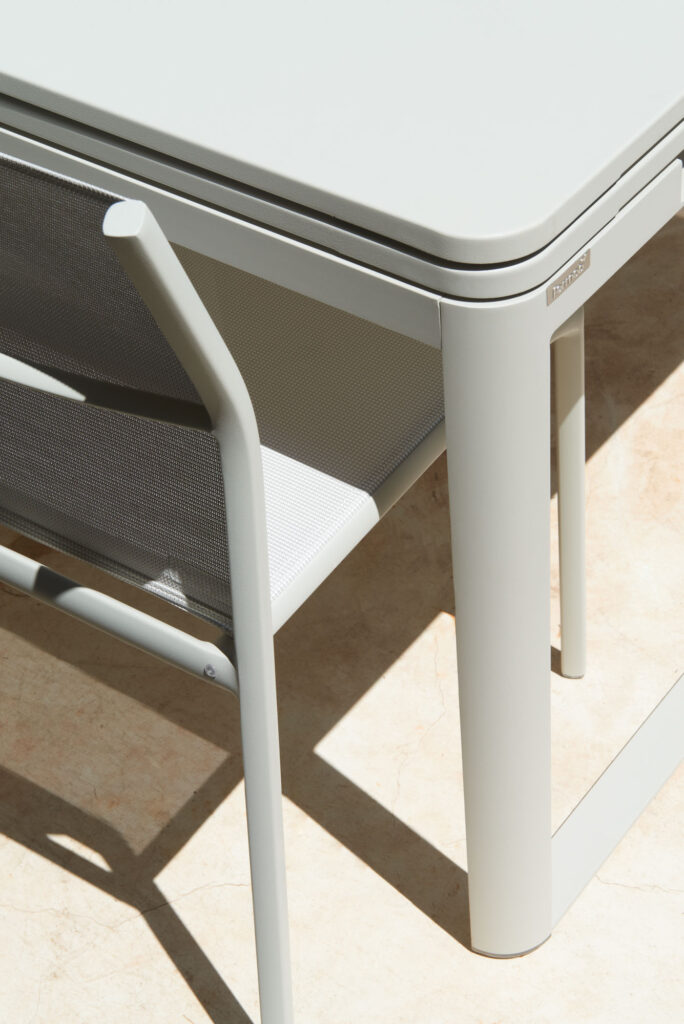 Une ambiance minimaliste et moderne : une chaise gris clair associée à une table extensible Biarritz sur un sol carrelé beige. Des cadres métalliques épurés rehaussent l'élégance et la fonctionnalité.