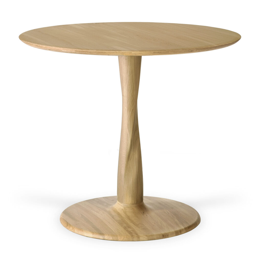 La table Torsion en chêne est dotée d'un plateau rond en chêne, d'une finition lisse en bois clair et d'un socle central, idéal pour les intérieurs polyvalents.