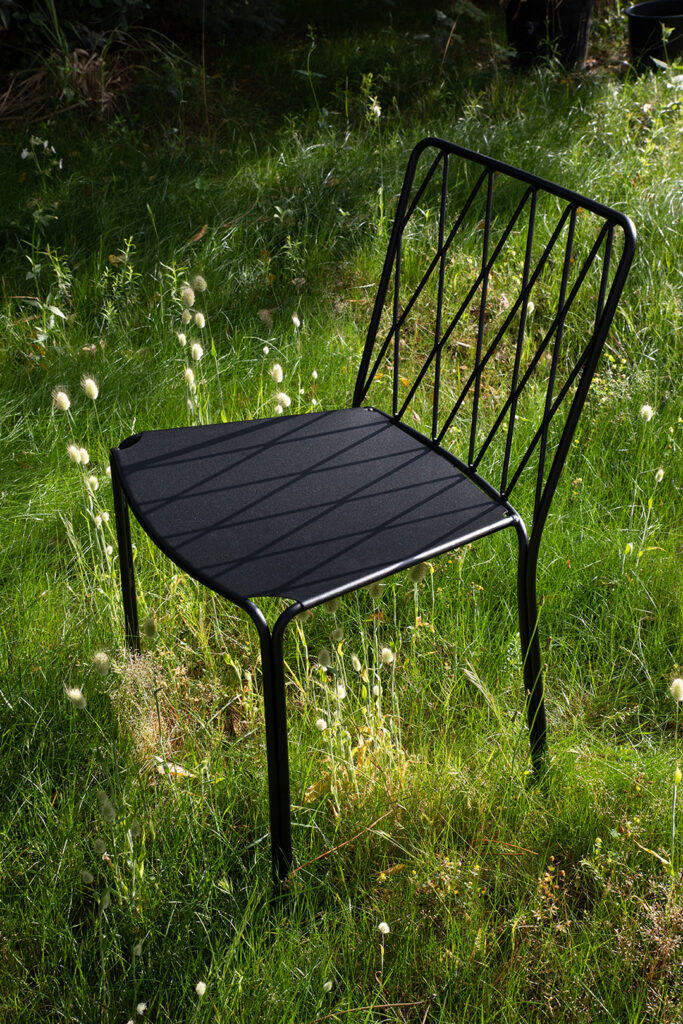 Une chaise en métal noir Chaise Kintbury, dotée de lignes verticales pour le soutien du dossier, est placée sur l'herbe dans un cadre extérieur ensoleillé.