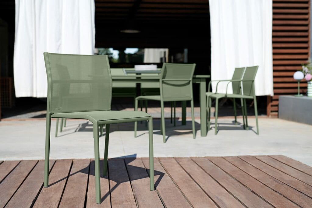 Coin repas extérieur avec chaises Harmony vertes sur une terrasse en bois, menant à une maison moderne avec portes coulissantes.