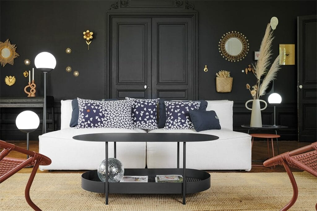 Salon élégant avec un canapé blanc, une table basse ronde noire Salsa et des chaises en osier contre un mur lambrissé sombre décoré de miroirs assortis et d'œuvres d'art murales.